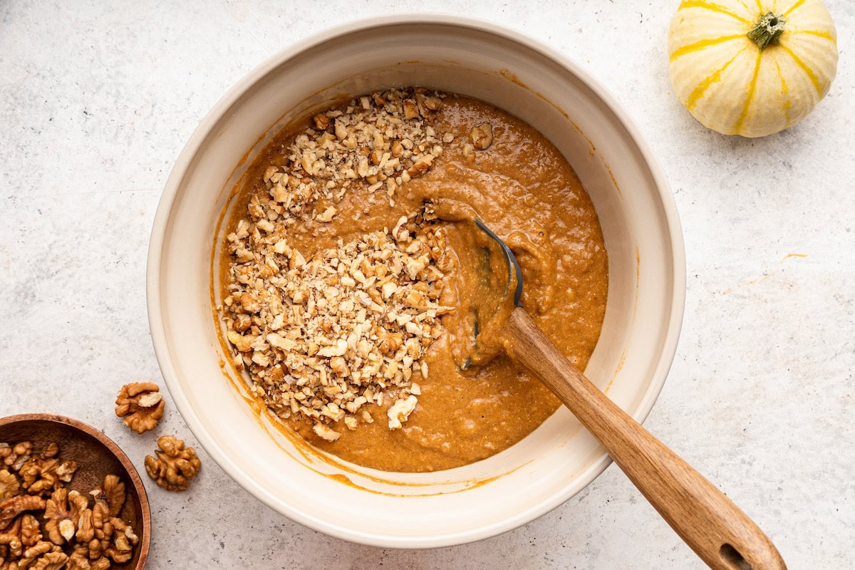 Crushed walnuts added to a bowl of pumpkin banana bread dough.
