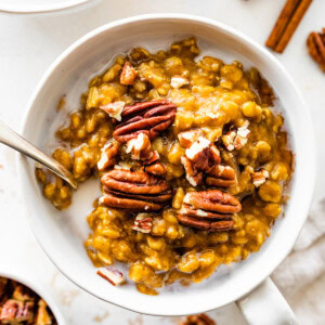 A bowl of pumpkin oatmeal with milk, and topped with pecans.