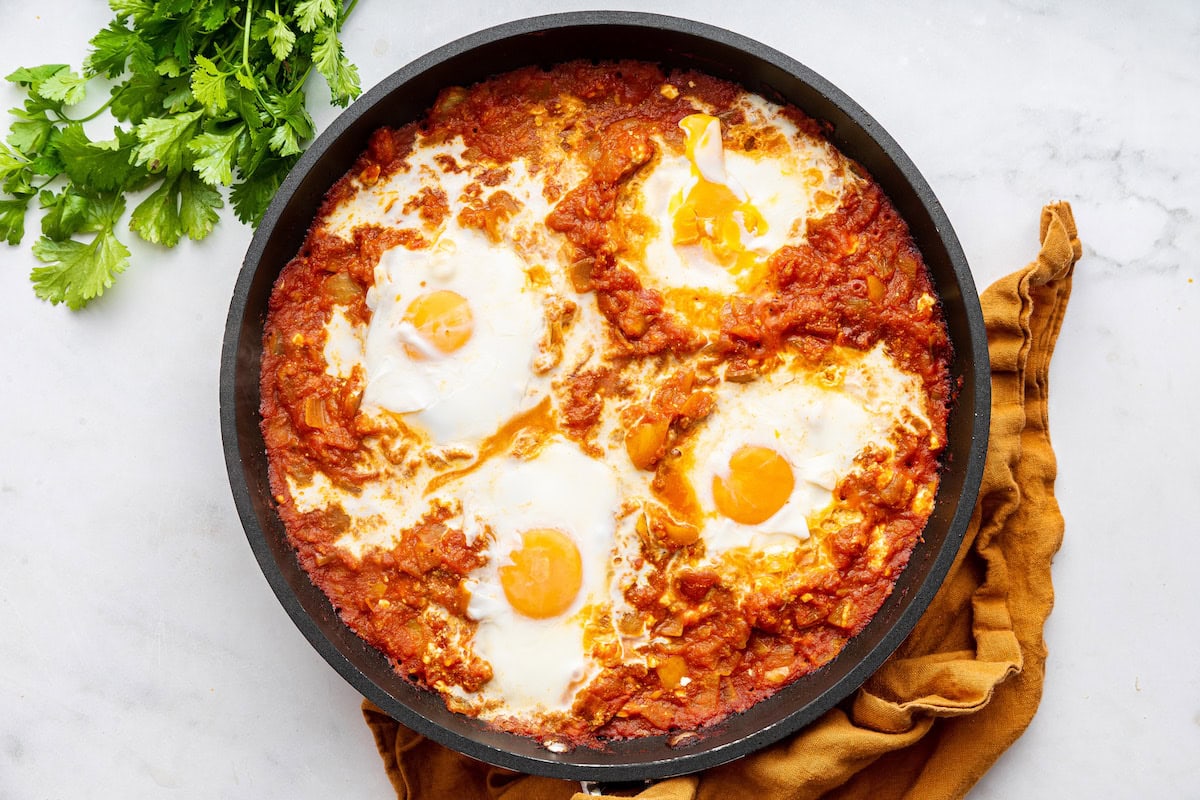 Four poached eggs in a pan with a tomato sauce.
