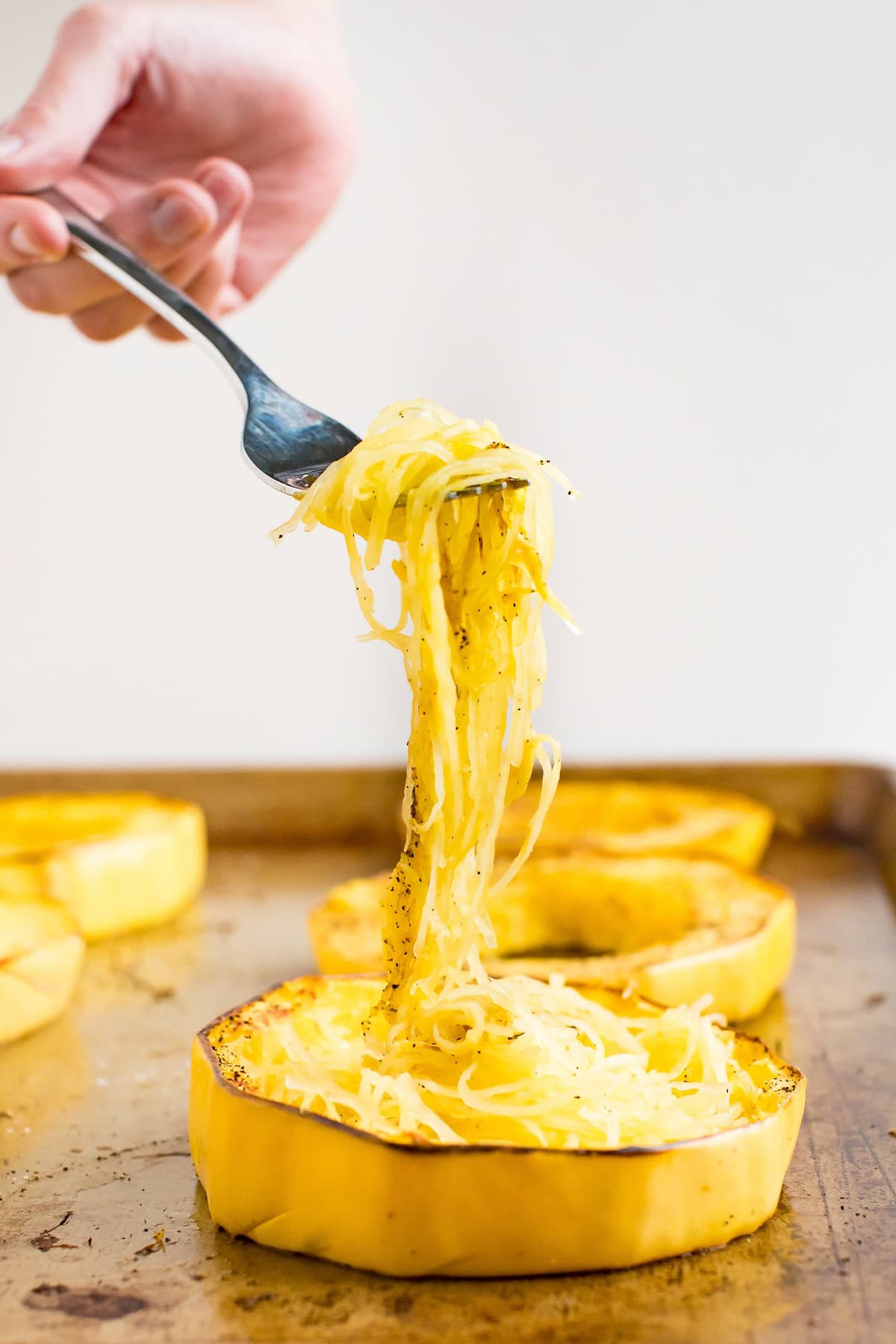 A woman's hand pulling spaghetti squash noodles out from a spaghetti squash ring.