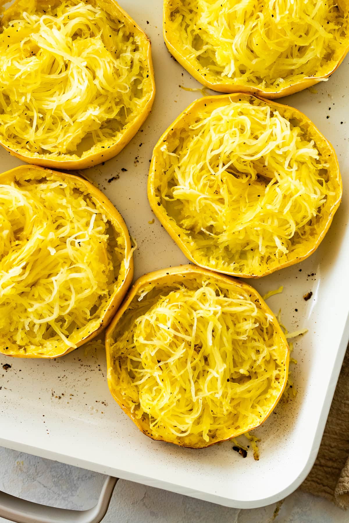 Roasted spaghetti squash rings in a white baking dish. The rings are shredded into long strands.