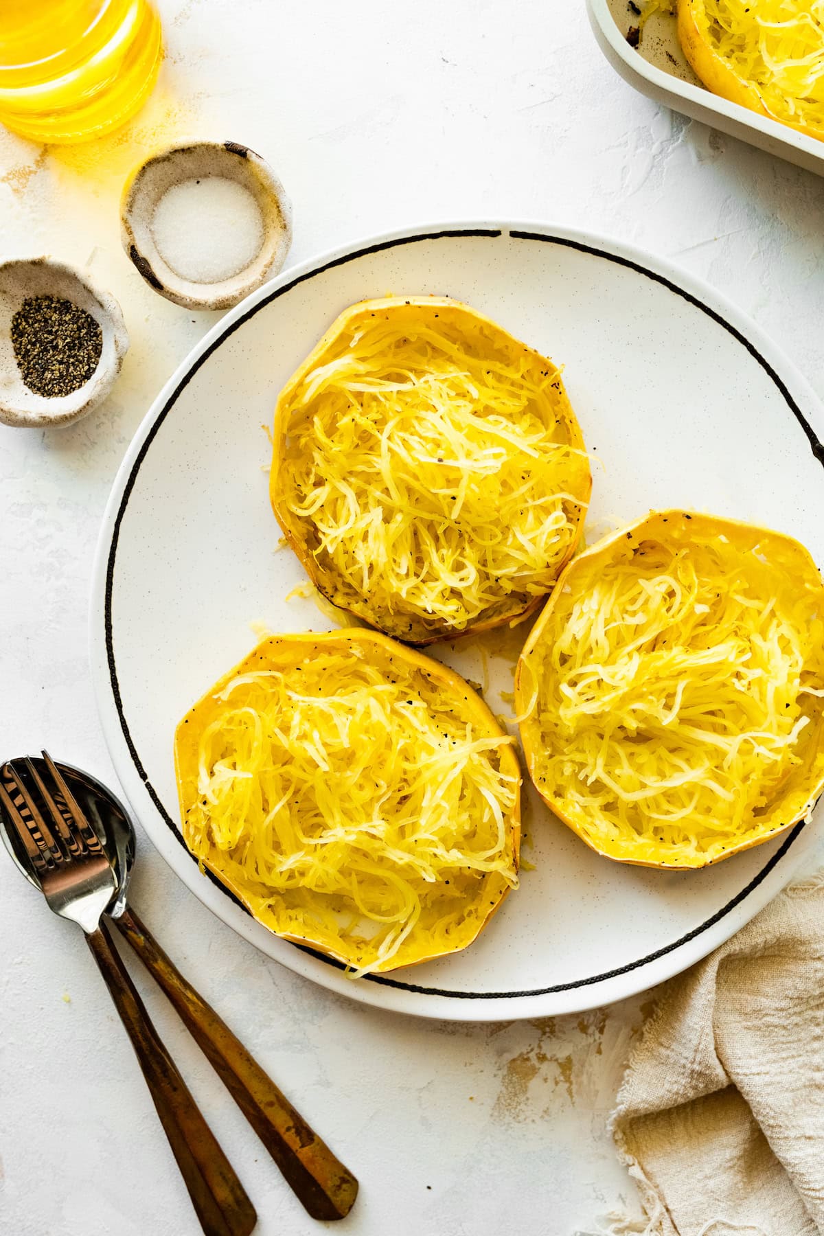 Three spaghetti squash rings on a white plate. The spaghetti squash is shredded into long strands.