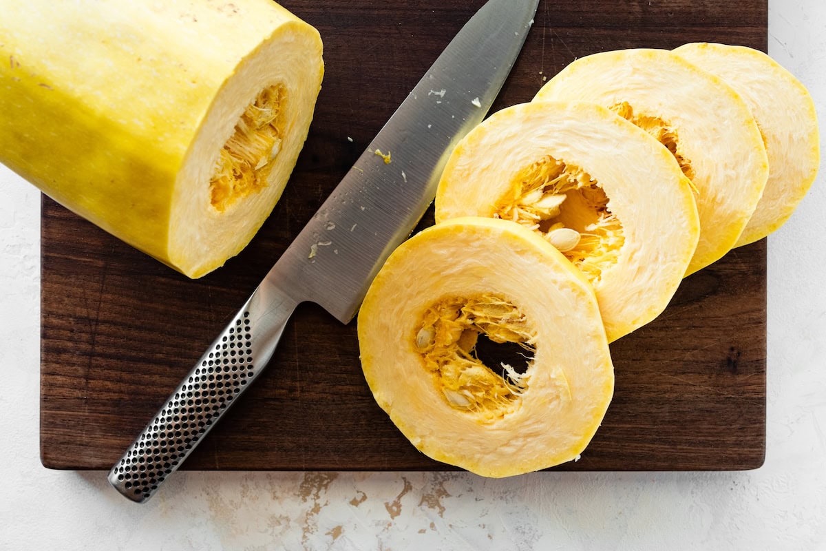A spaghetti squash on a wooden cutting board being cut into rings with a knife.
