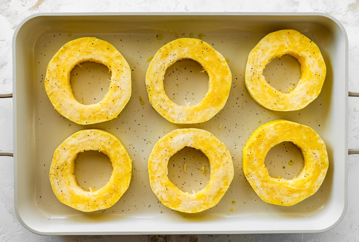 Six round spaghetti squash rings in a baking pan sprinkled with salt and pepper.