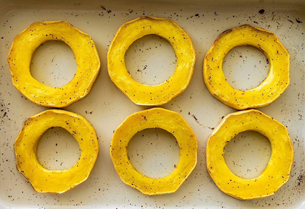 Six round roasted spaghetti squash rings in a baking pan sprinkled with salt and pepper.