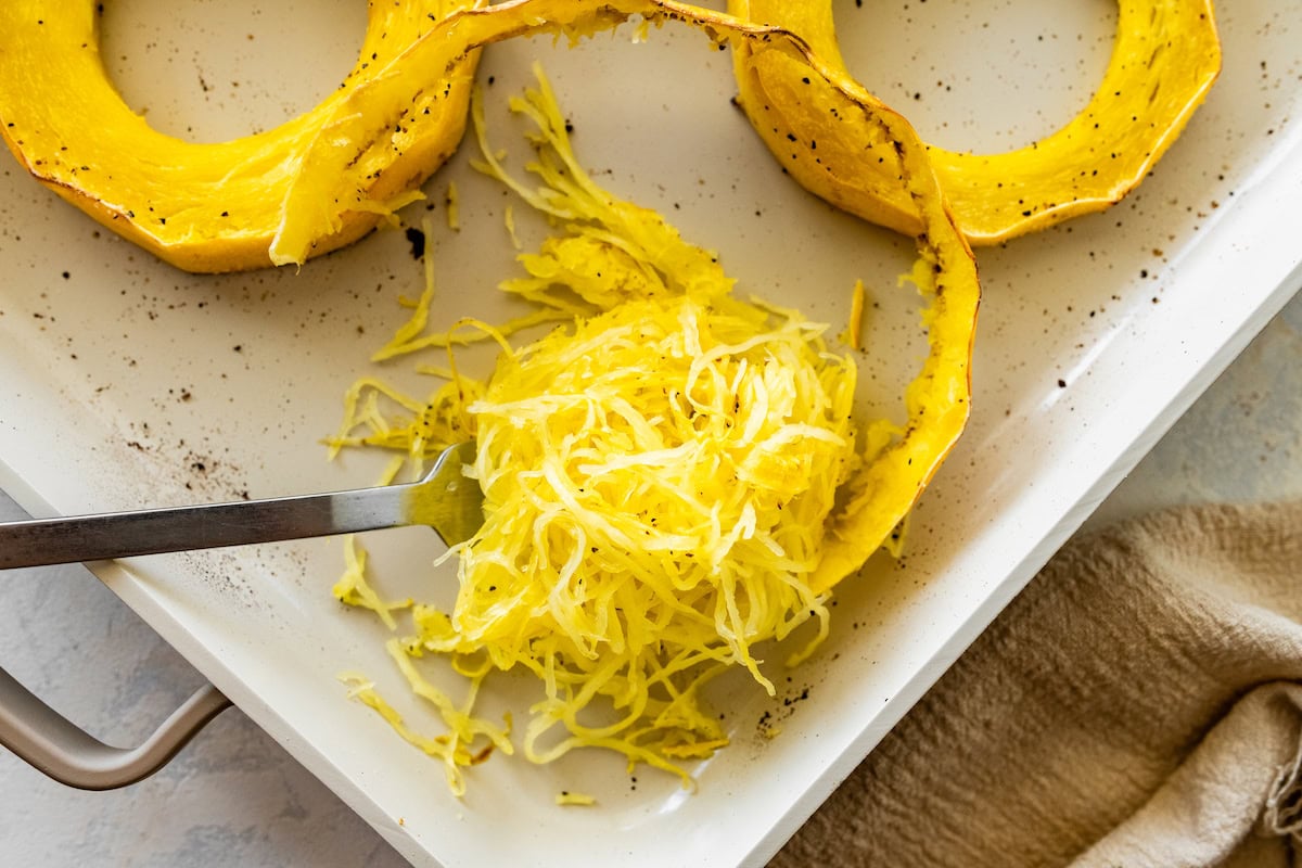 A fork shredding a spaghetti squash ring into long strands.