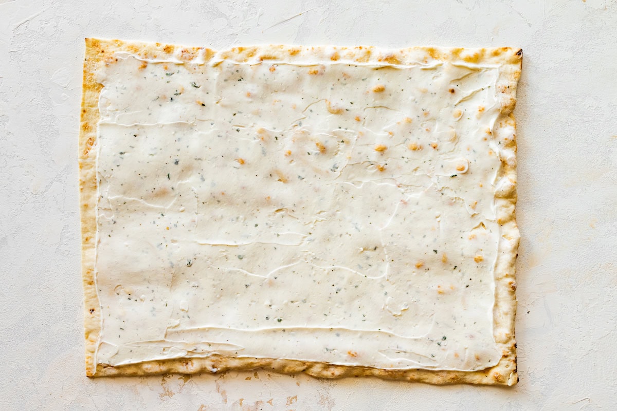 A cream cheese, yogurt, and ranch seasoning mixture spread on a piece of flatbread.