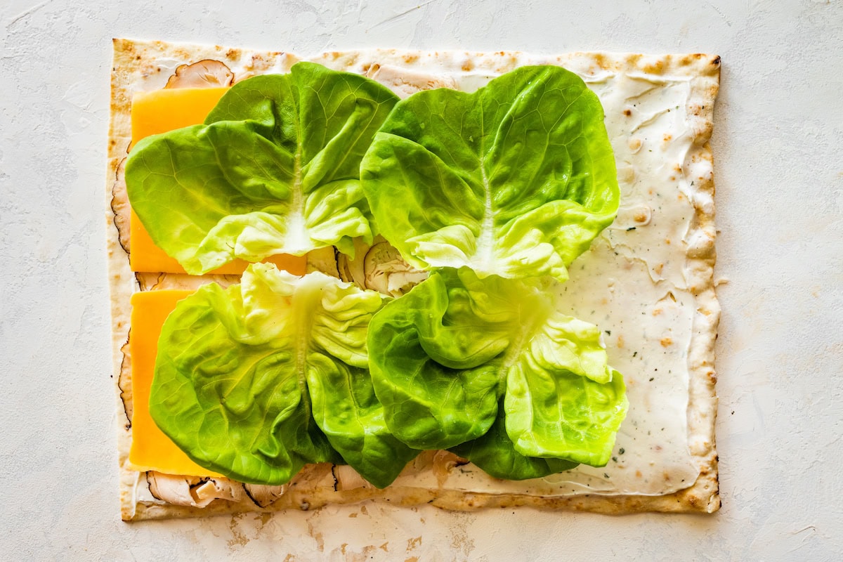 Cheese, lettuce and turkey added to a piece of flatbread with a cream cheese mixture on the bread.