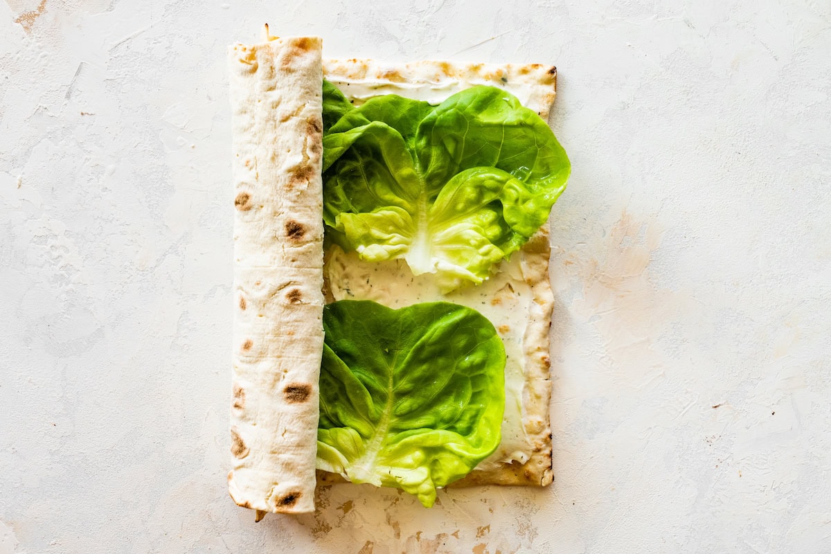 Rolling a piece of flatbread with turkey, lettuce, cheese, and cream cheese.