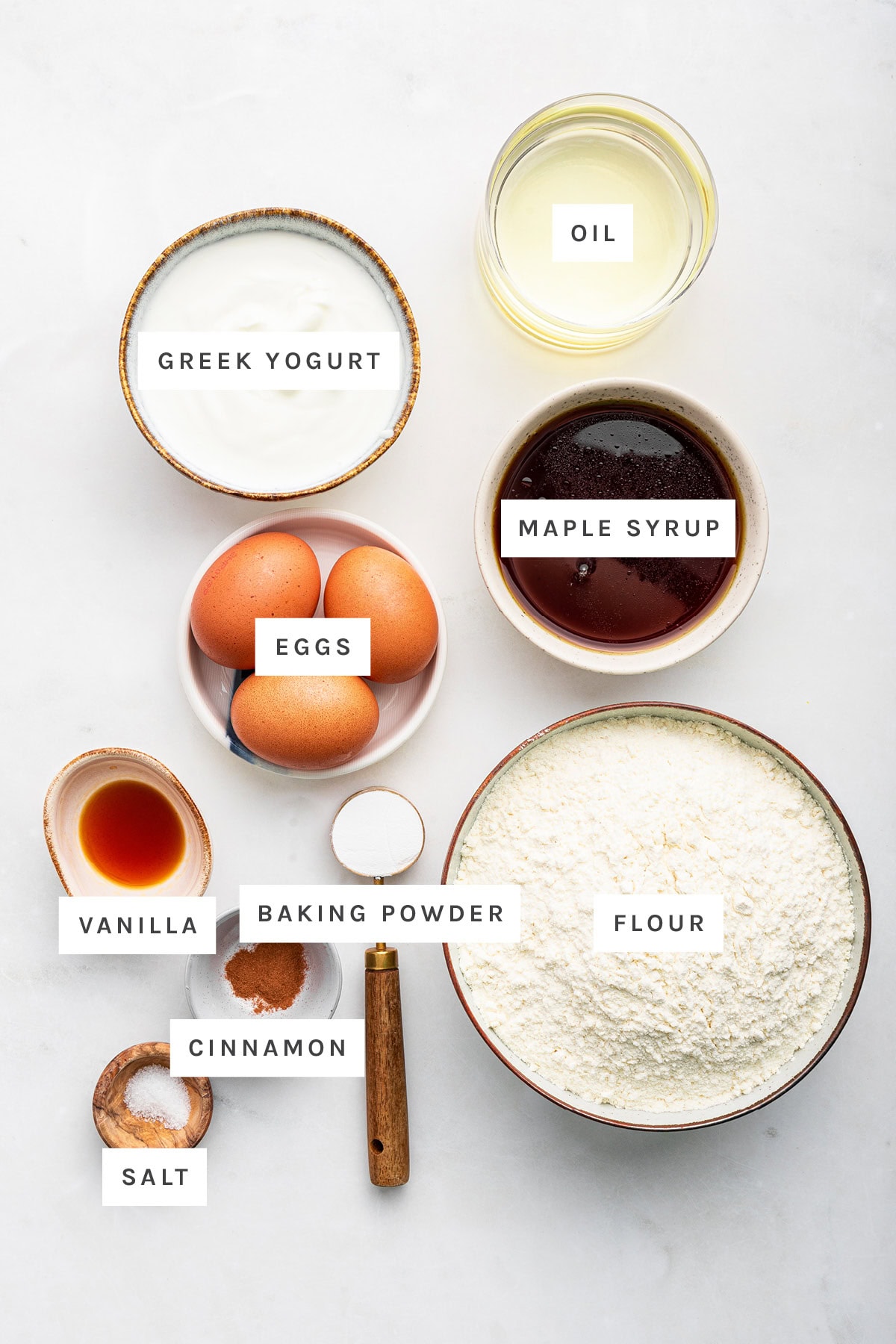 Ingredients measured out to make French Yogurt Cake: Greek yogurt, oil, maple syrup, eggs, vanilla, baking powder, flour, cinnamon and salt.