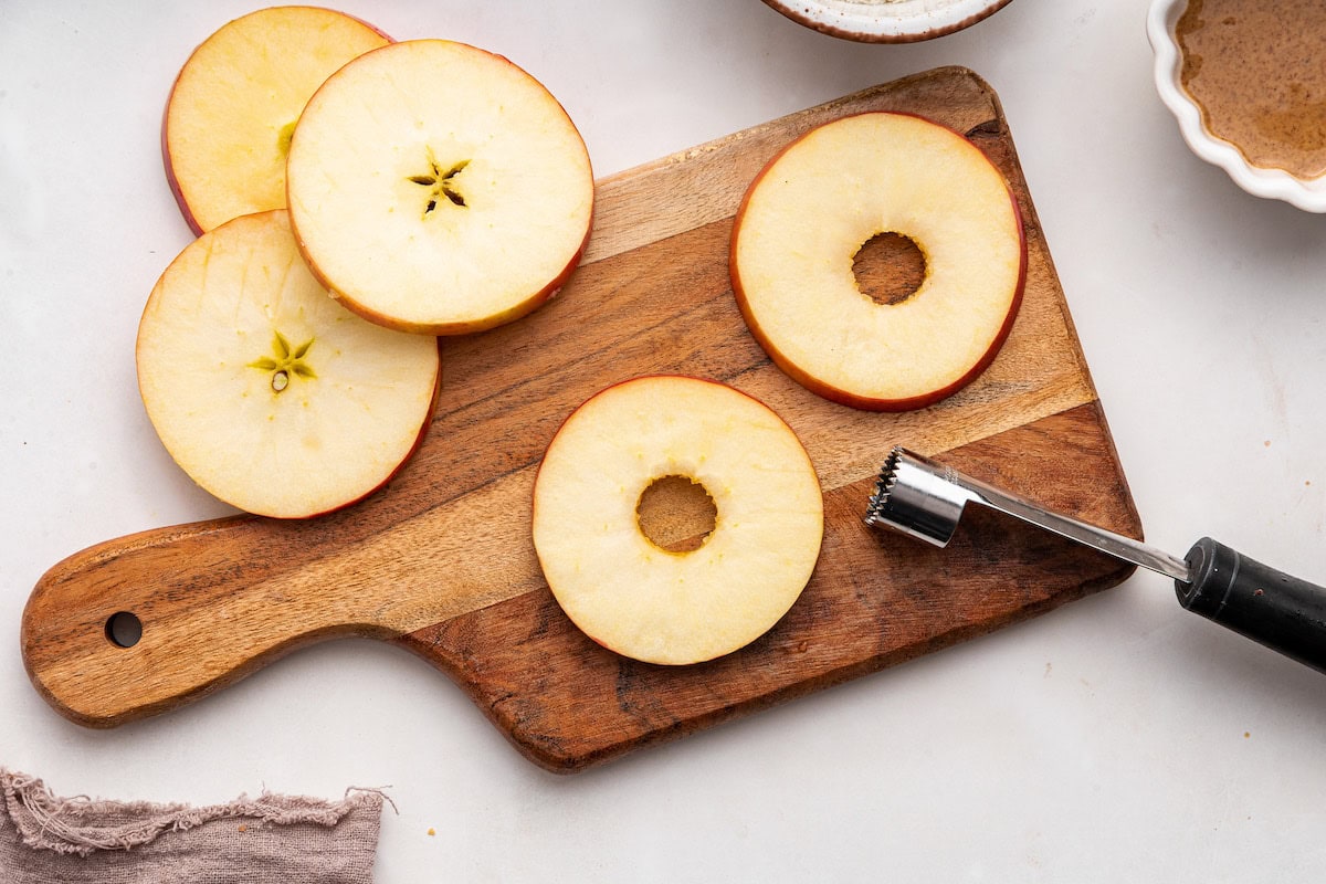 Circular apple slices with the core taken out on a cutting board.
