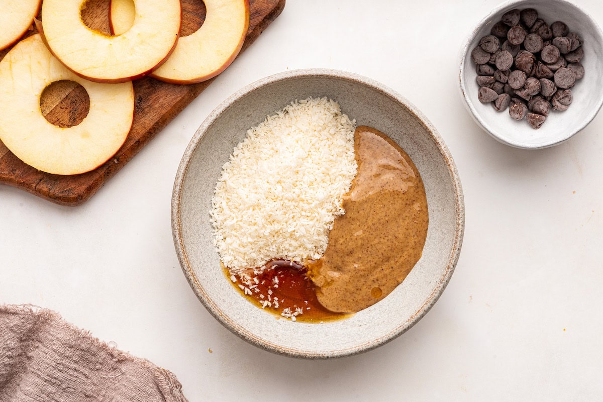 A bowl of almond butter, maple syrup, and coconut shreds.