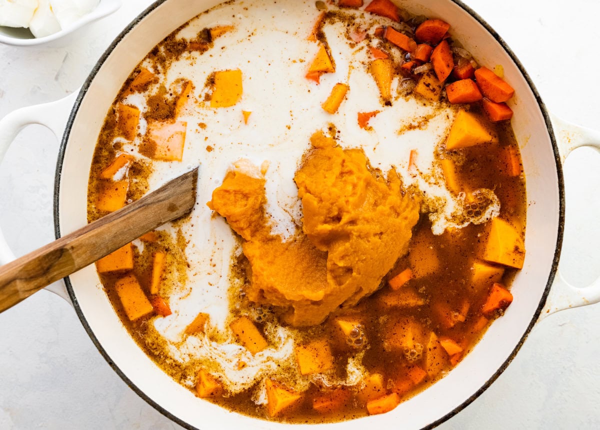 Coconut milk and pumpkin puree added to a large pot of autumn soup.