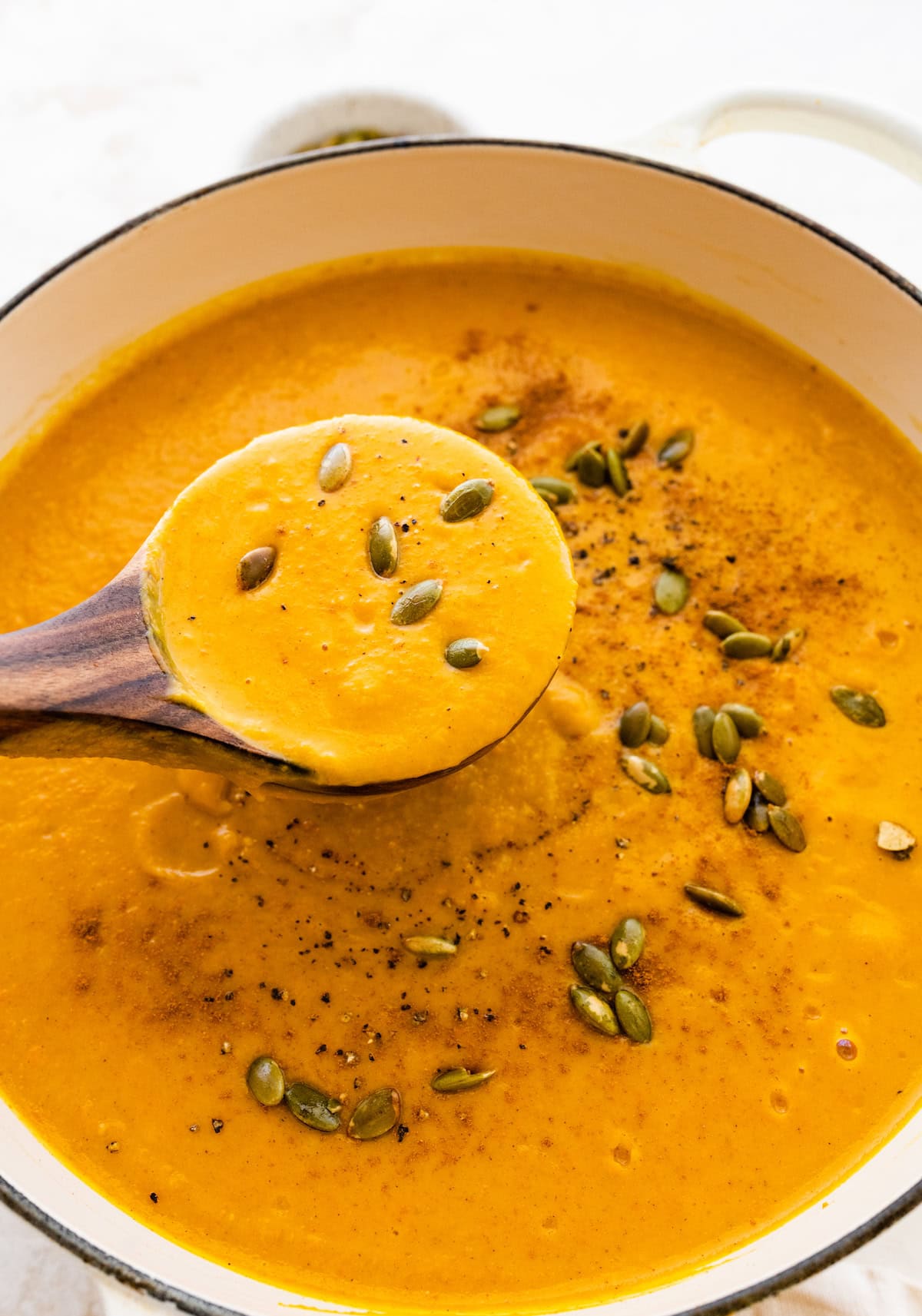 An autumn soup in a bowl topped with pepitas and black pepper.