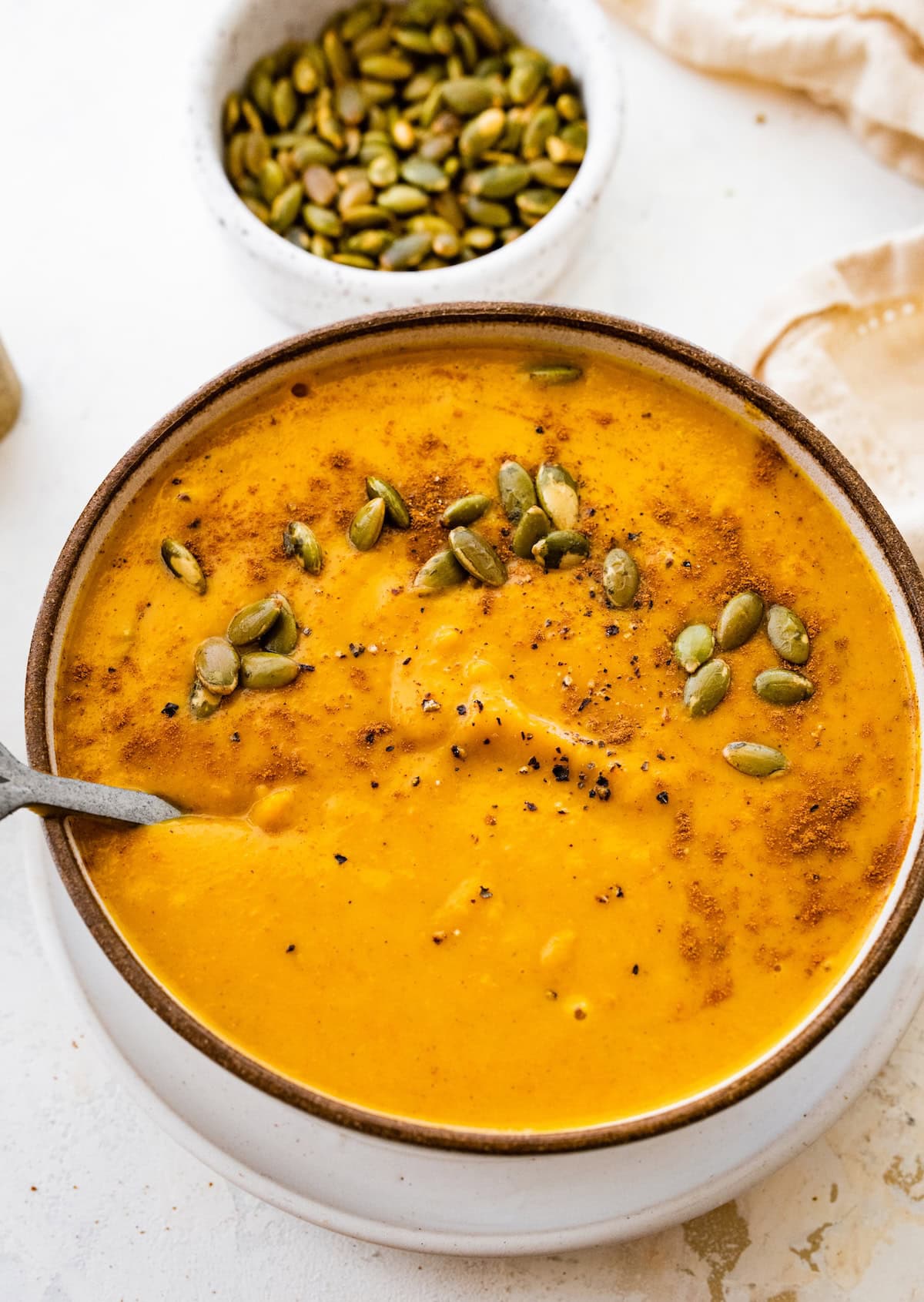 A bowl of autumn soup topped with cracked black pepper, and pepitas.