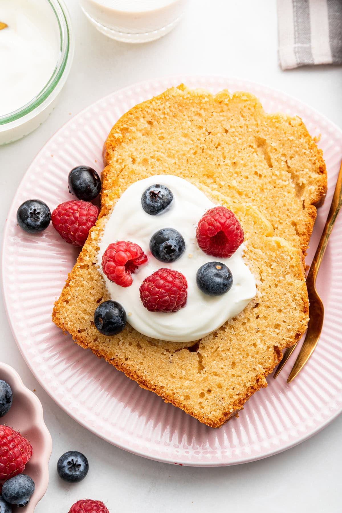 Two slices of french yogurt cake on a plate. One slice is topped with a dollop of yogurt and fresh berries.