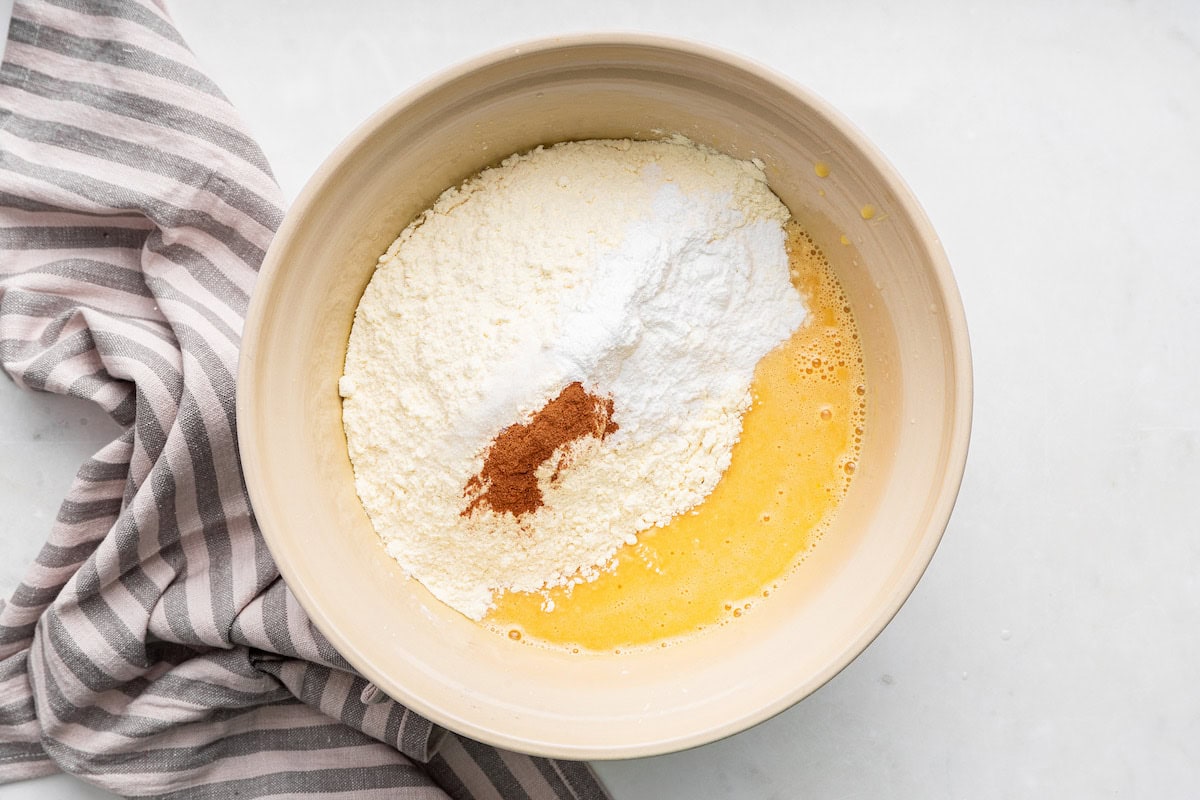 Flour, cinnamon, and baking soda added to a large bowl of wet ingredients used for a french yogurt cake.