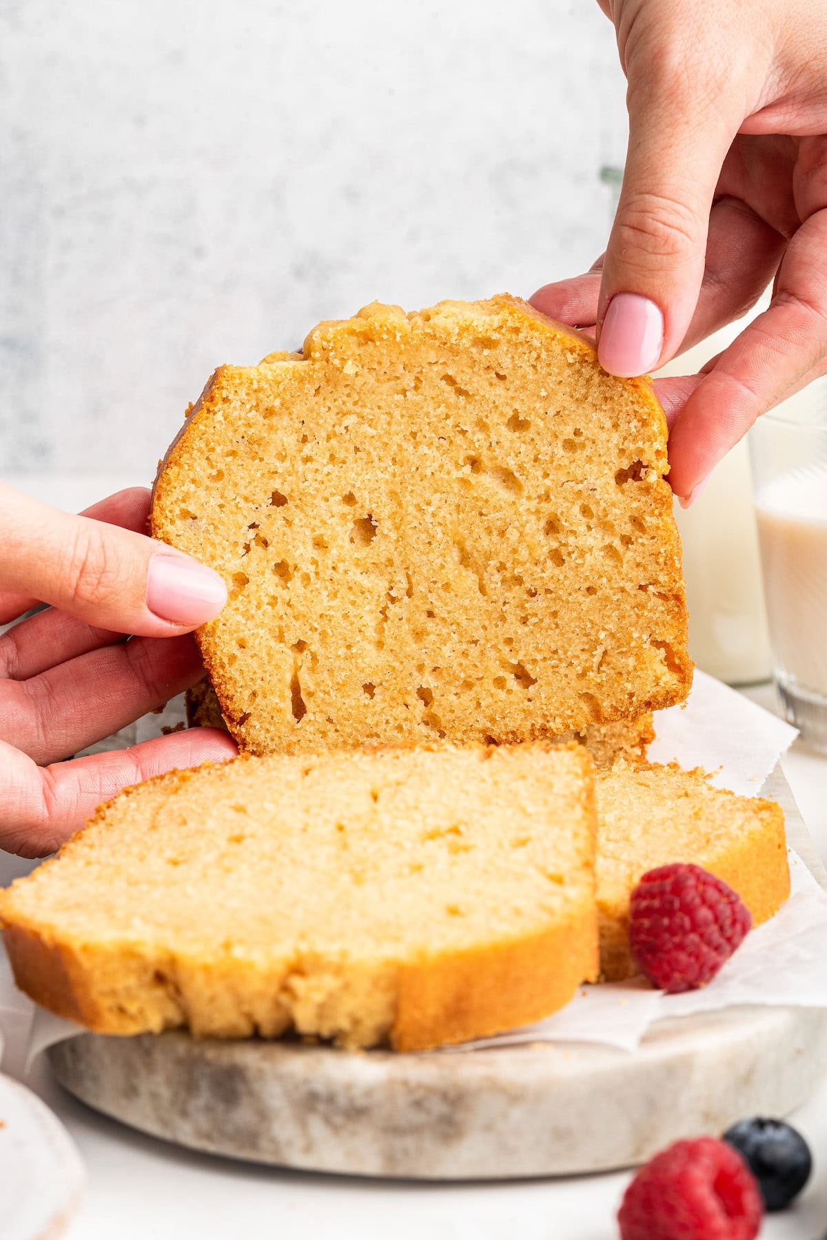 A woman's hands hold a slice of french yogurt cake near other slices.
