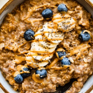 A serving of peanut butter oatmeal in a bowl topped with sliced banana, fresh blueberries, chia, and a drizzle of peanut butter.
