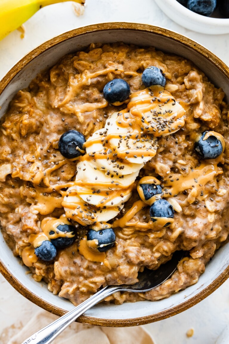 A serving of peanut butter oatmeal in a bowl topped with sliced banana, fresh blueberries, chia, and a drizzle of peanut butter.