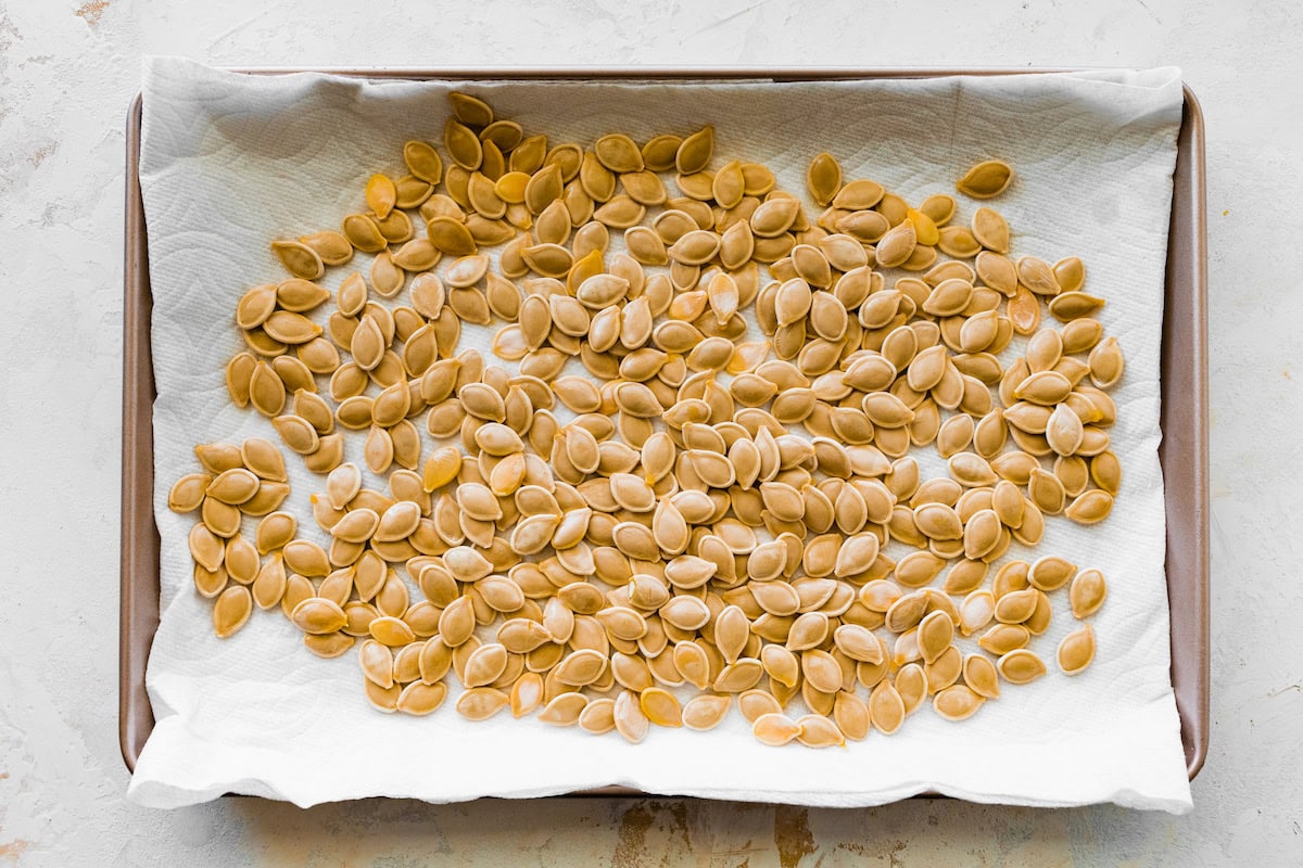 Dried pumpkin seeds spread out on a paper towel on a baking sheet.