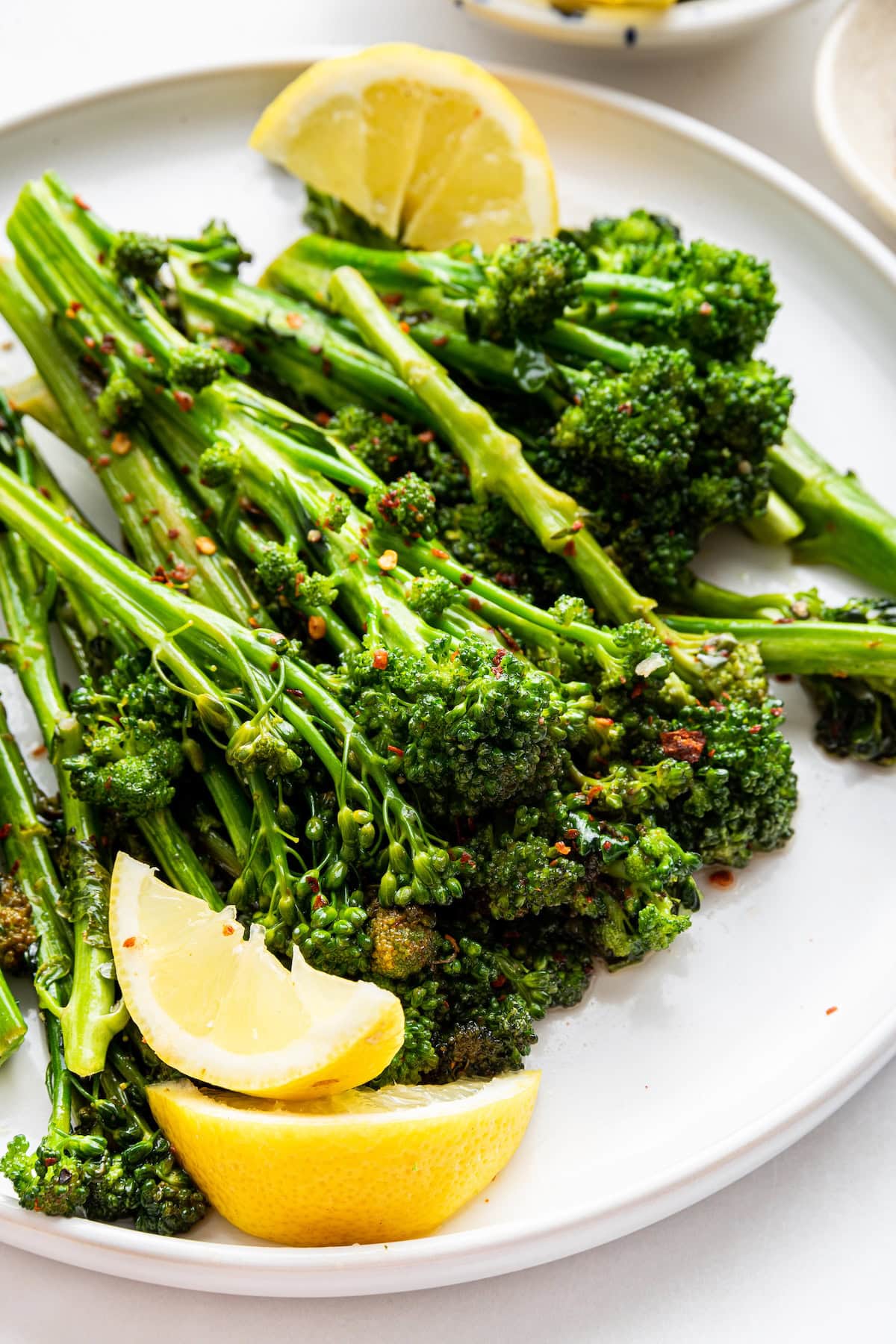 A plate of sautéed broccolini garnished with red pepper flakes and lemon wedges on the side.
