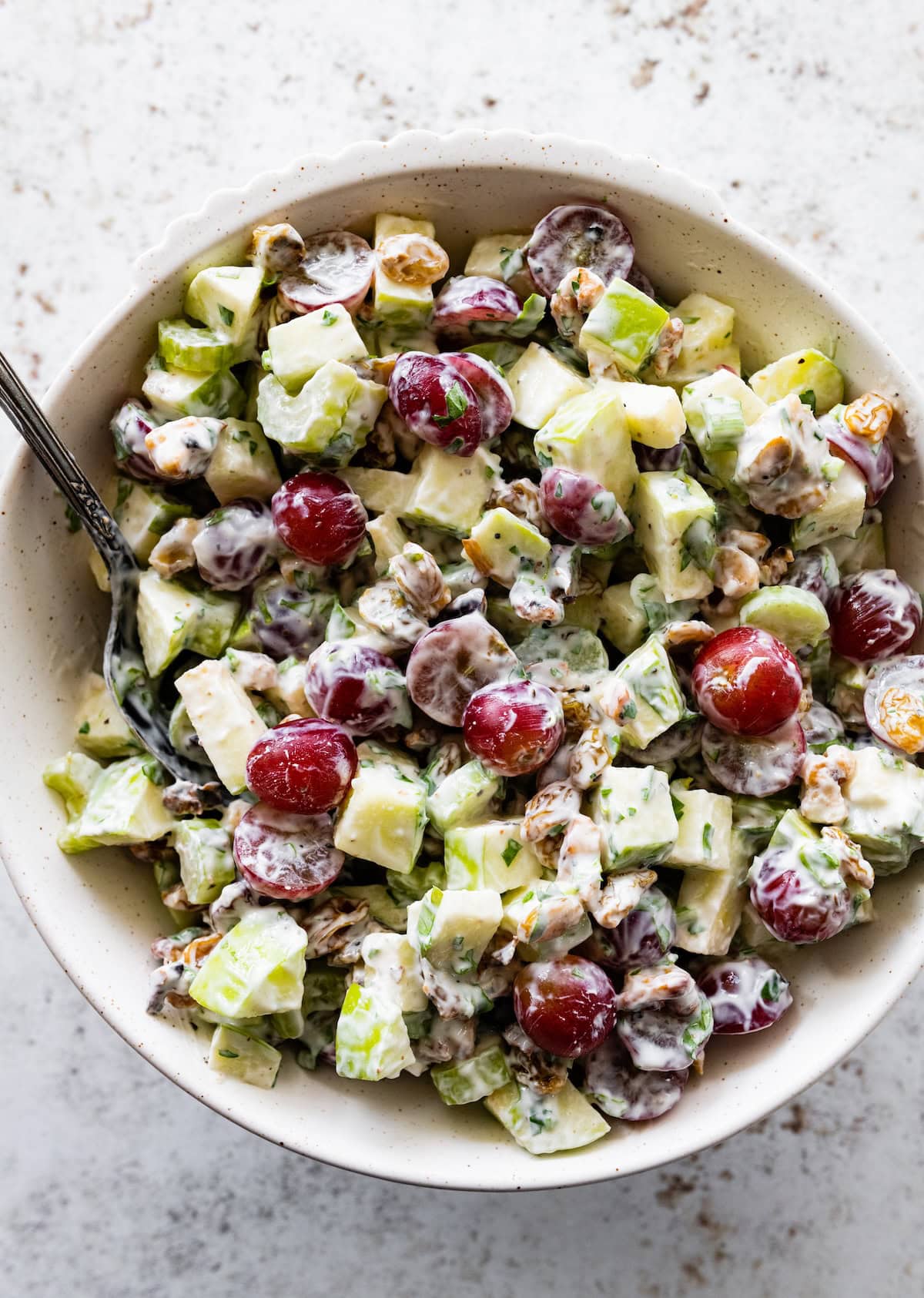 A waldorf salad served in a white bowl with a silver spoon.