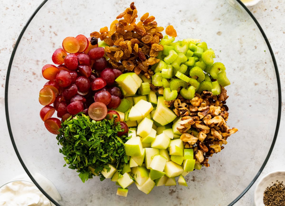 Walnuts, celery, raisins, grapes, apples, and fresh parsley in a glass bowl.