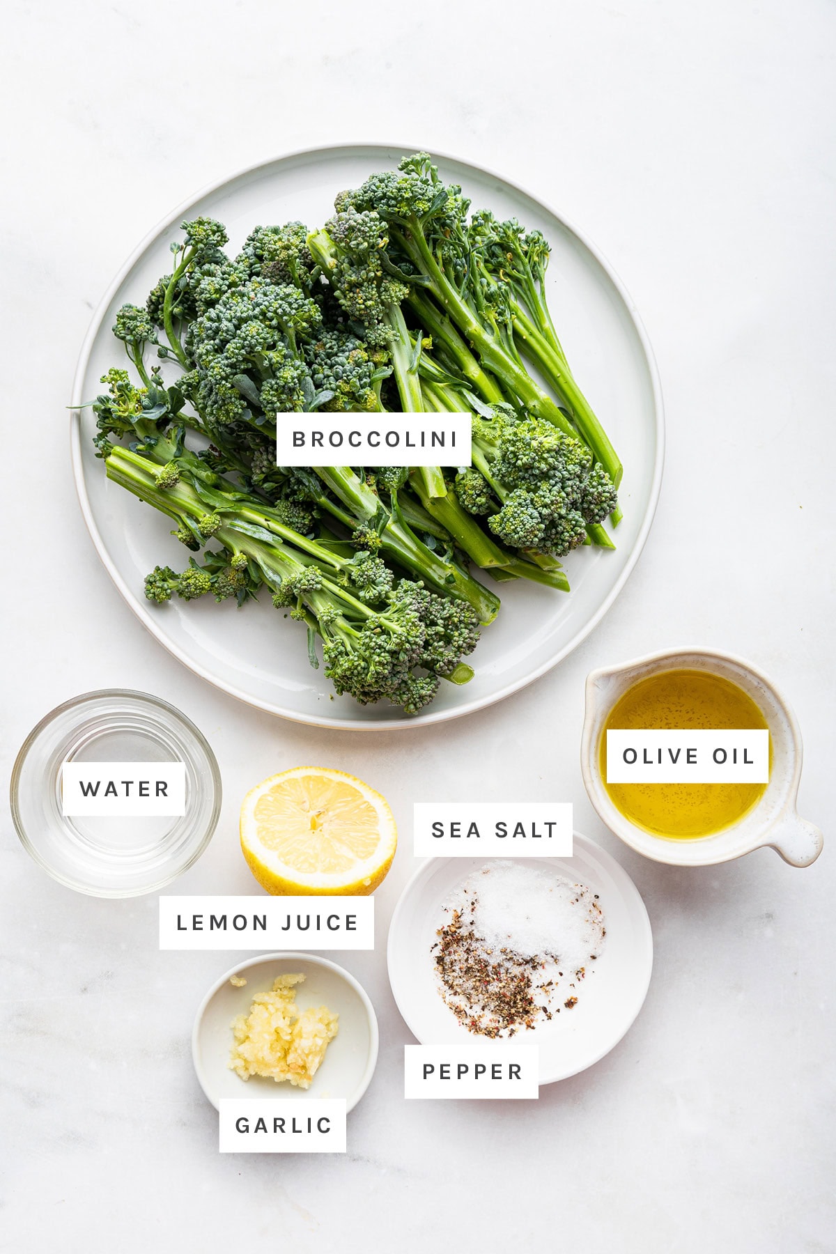 Ingredients measured out to make Sautéed Broccolini: broccolini, water, lemon juice, garlic, sea salt, pepper and olive oil.