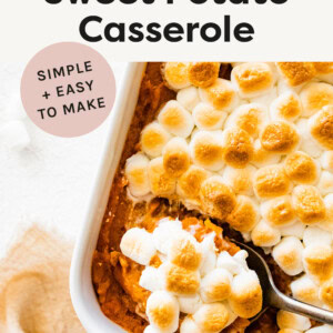 Sweet potato casserole topped with marshmallows. A spoon is scooping out a portion in the pan.