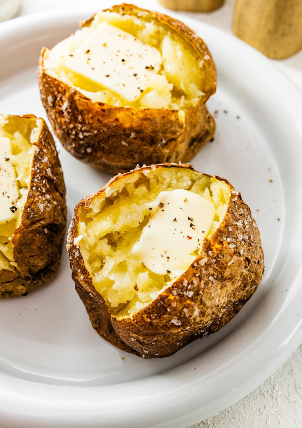 Three air fryer baked potatoes split open on a plate with slices of butter and seasoning.