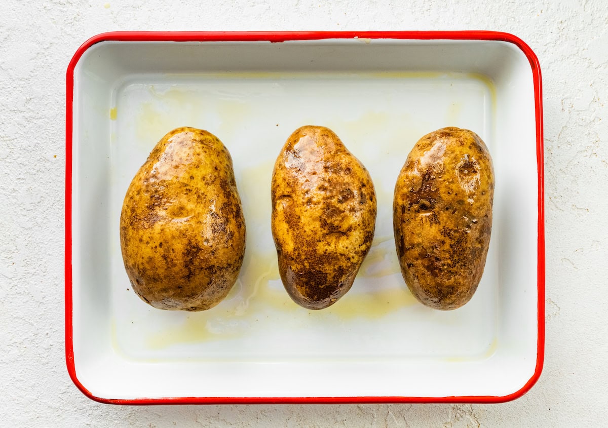 Three potatoes covered in oil in a baking dish.