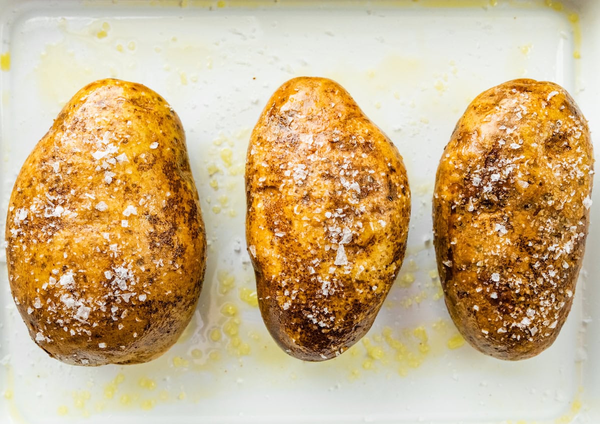 Three potatoes covered in oil and salt in a baking dish.