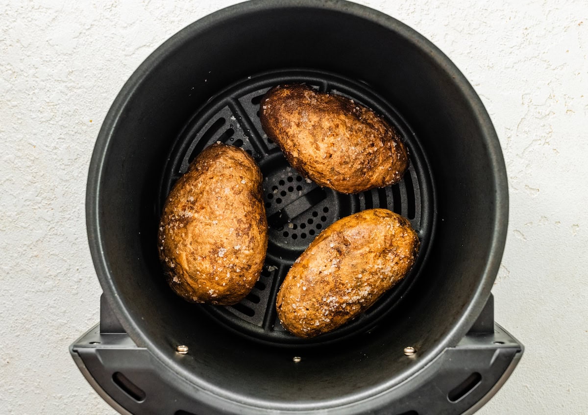 Three potatoes covered in oil and salt in and air fryer basket.