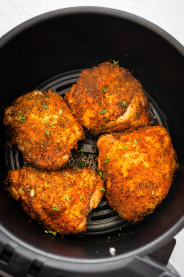 Four bone-in chicken thighs cooked in the basket of an air fryer topped with fresh parsley.