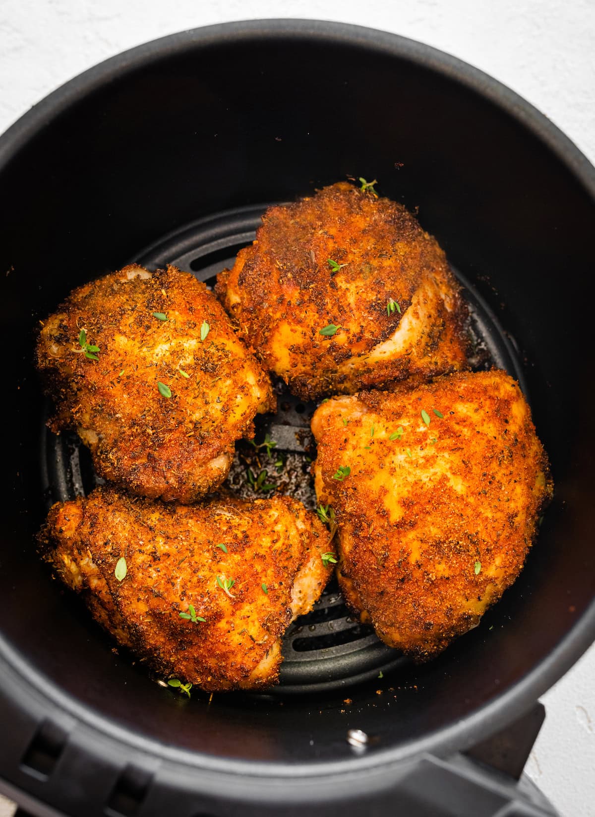 air fryer chicken thighs Four bone-in chicken thighs cooked in the basket of an air fryer topped with fresh parsley.