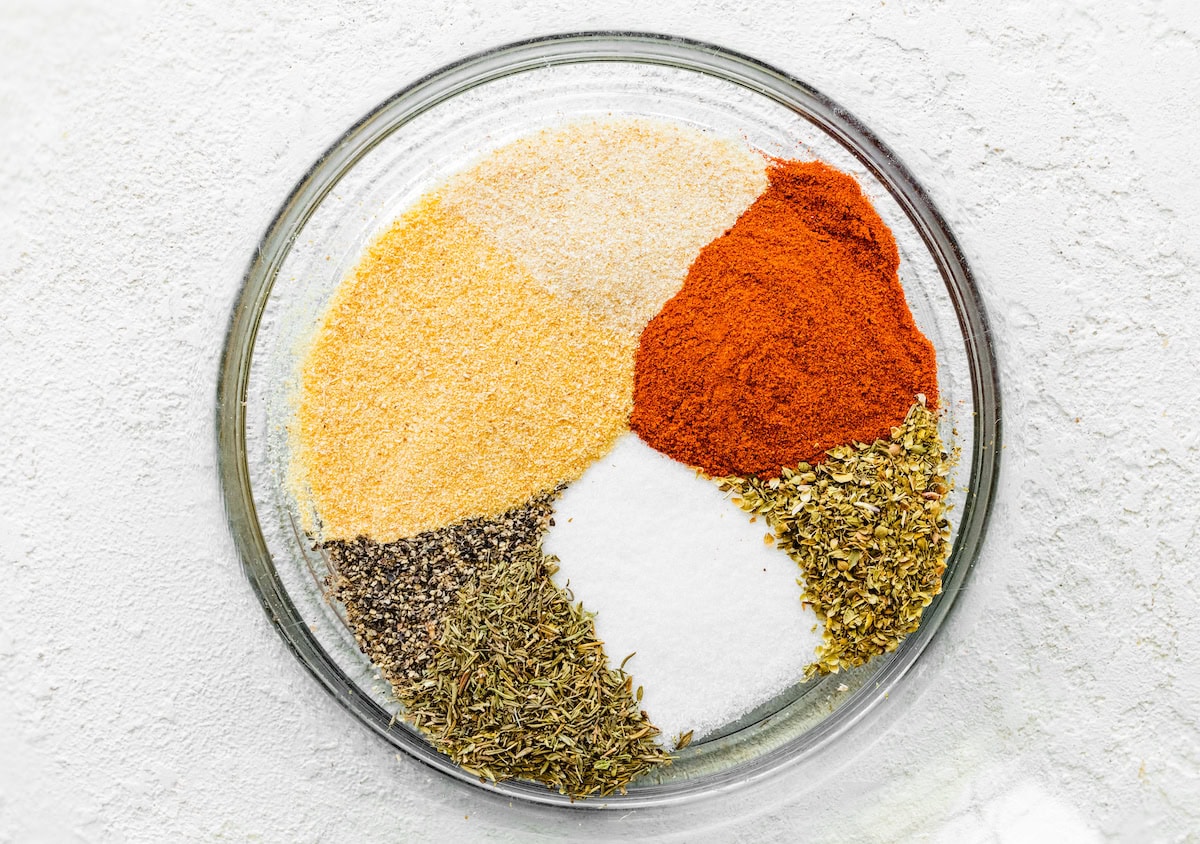 A blend of seasonings in a glass mixing bowl: garlic powder, onion powder, paprika, oregano, thyme, salt and pepper.