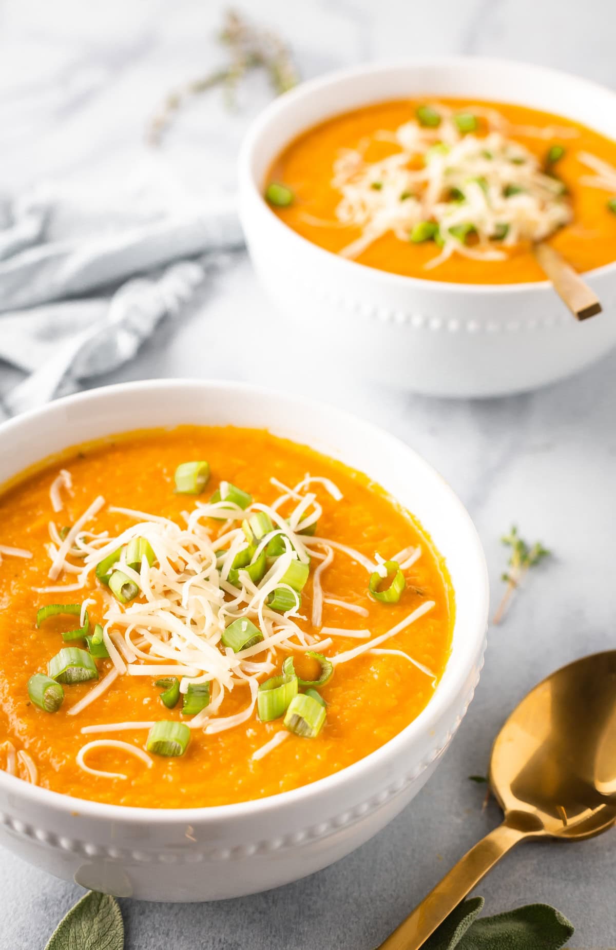 Two bowls of carrot parsnip soup garnished with scallions and gruyere cheese.