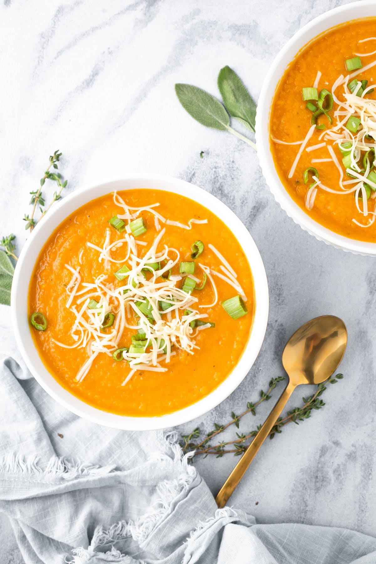 Two servings of carrot parsnip soup garnished with scallions and shredded gruyere cheese.