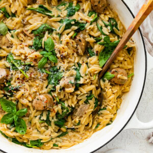 A white Dutch oven with creamy orzo, chicken sausage and spinach mixed together.