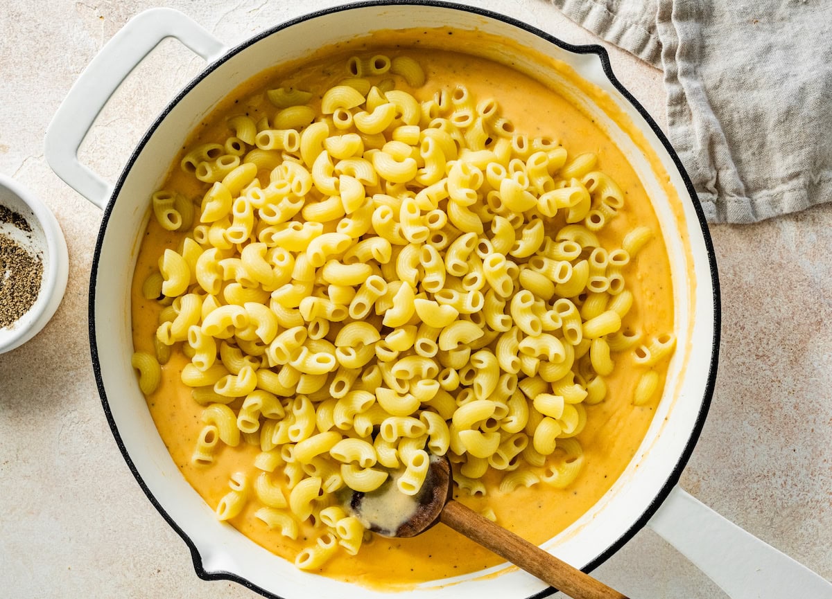 Macaroni noodles added to a large pot of cottage cheese sauce.