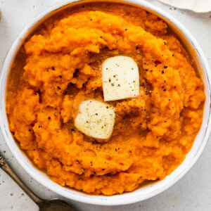 A bowl of mashed sweet potatoes topped with black pepper and slices of butter.