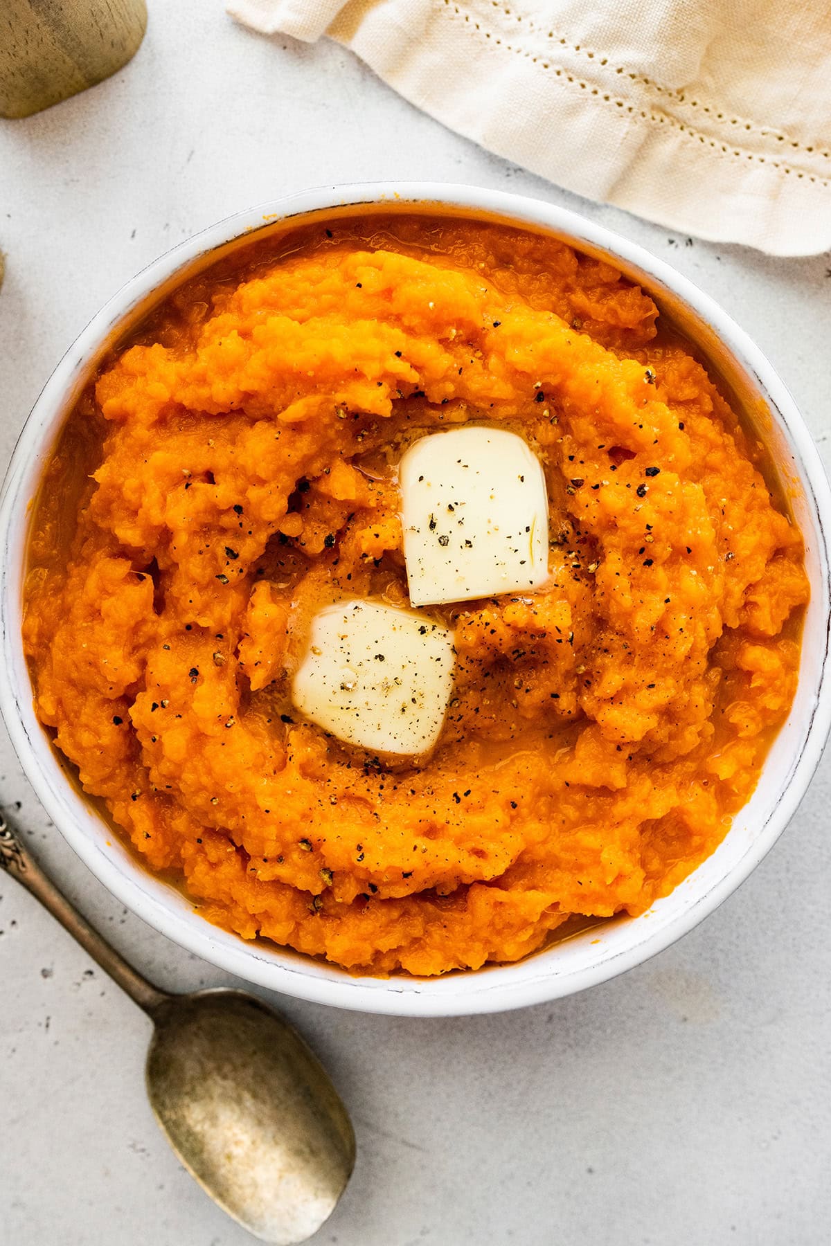 A bowl of mashed sweet potatoes topped with black pepper and slices of butter.