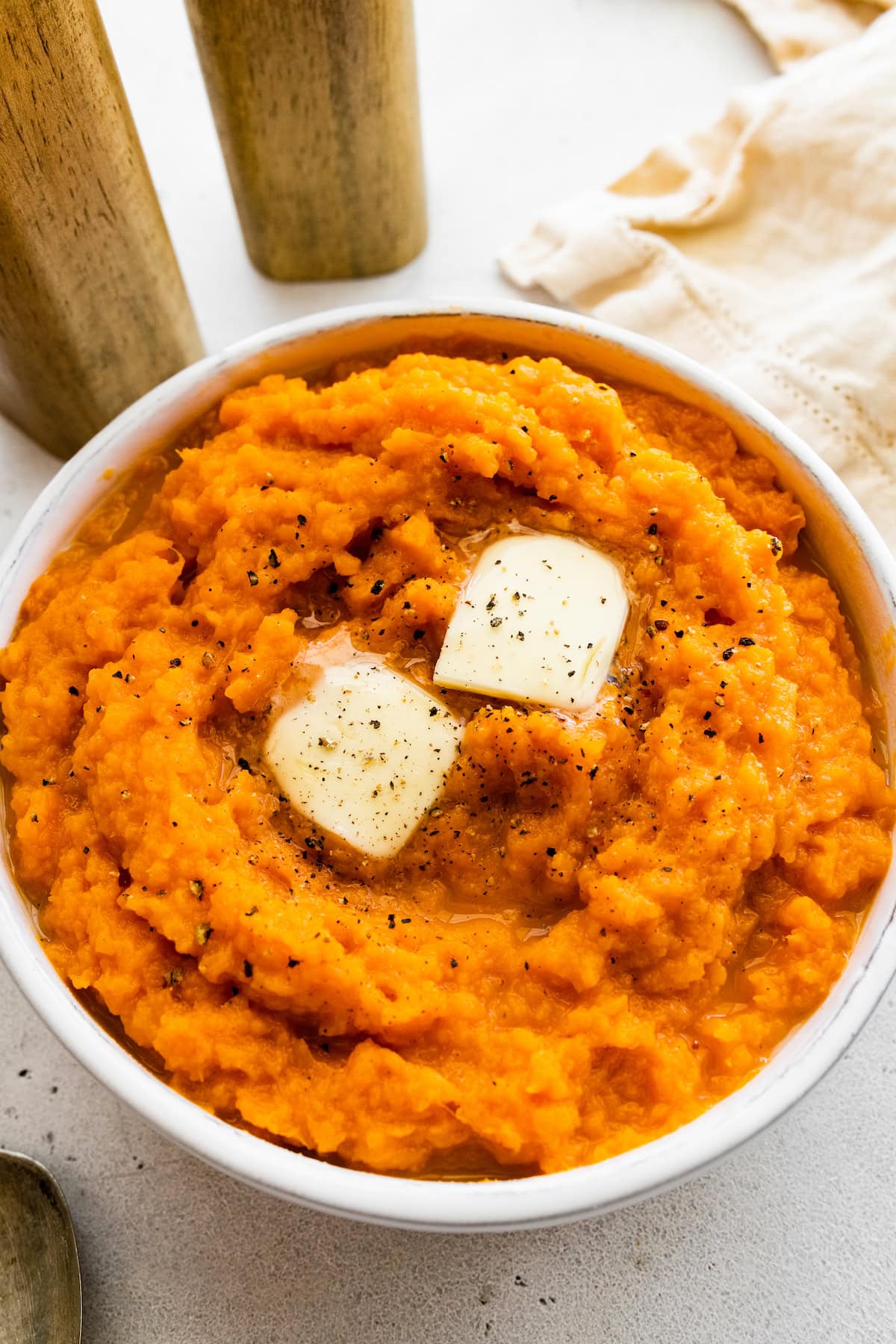 A bowl with sweet mashed potatoes with butter, and black pepper.