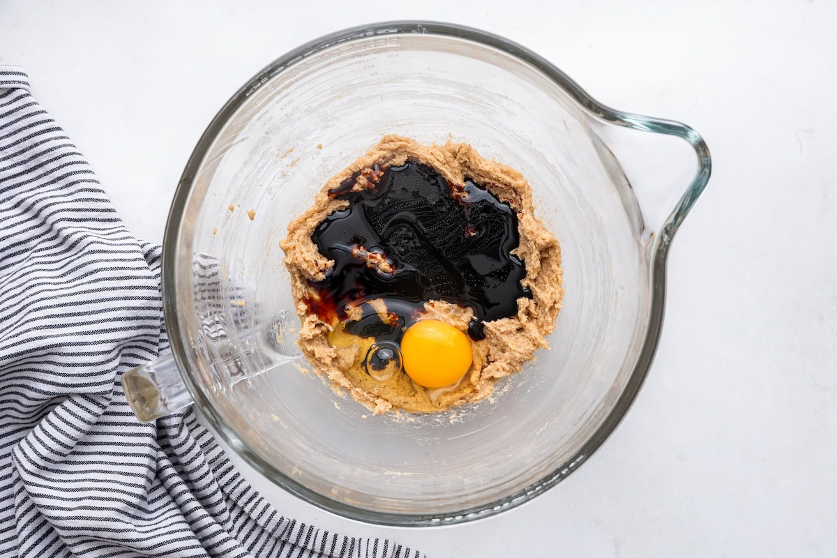 Molasses and an egg being added to the wet ingredients for the molasses cookies in a glass bowl.