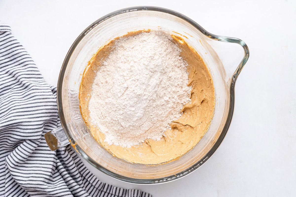 The dry ingredients being added to the wet ingredients for the molasses cookies in a glass mixing bowl.