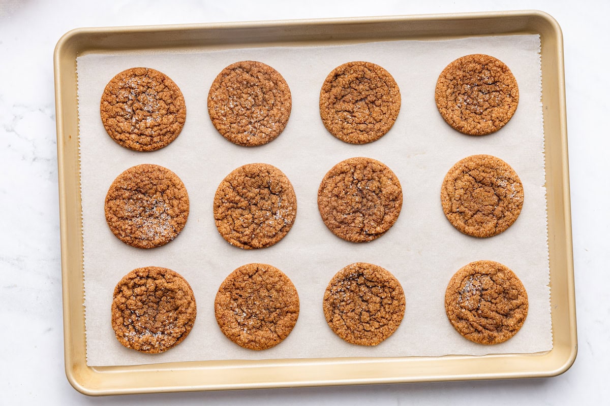 Baked molasses cookies on a baking sheet with parchment paper.