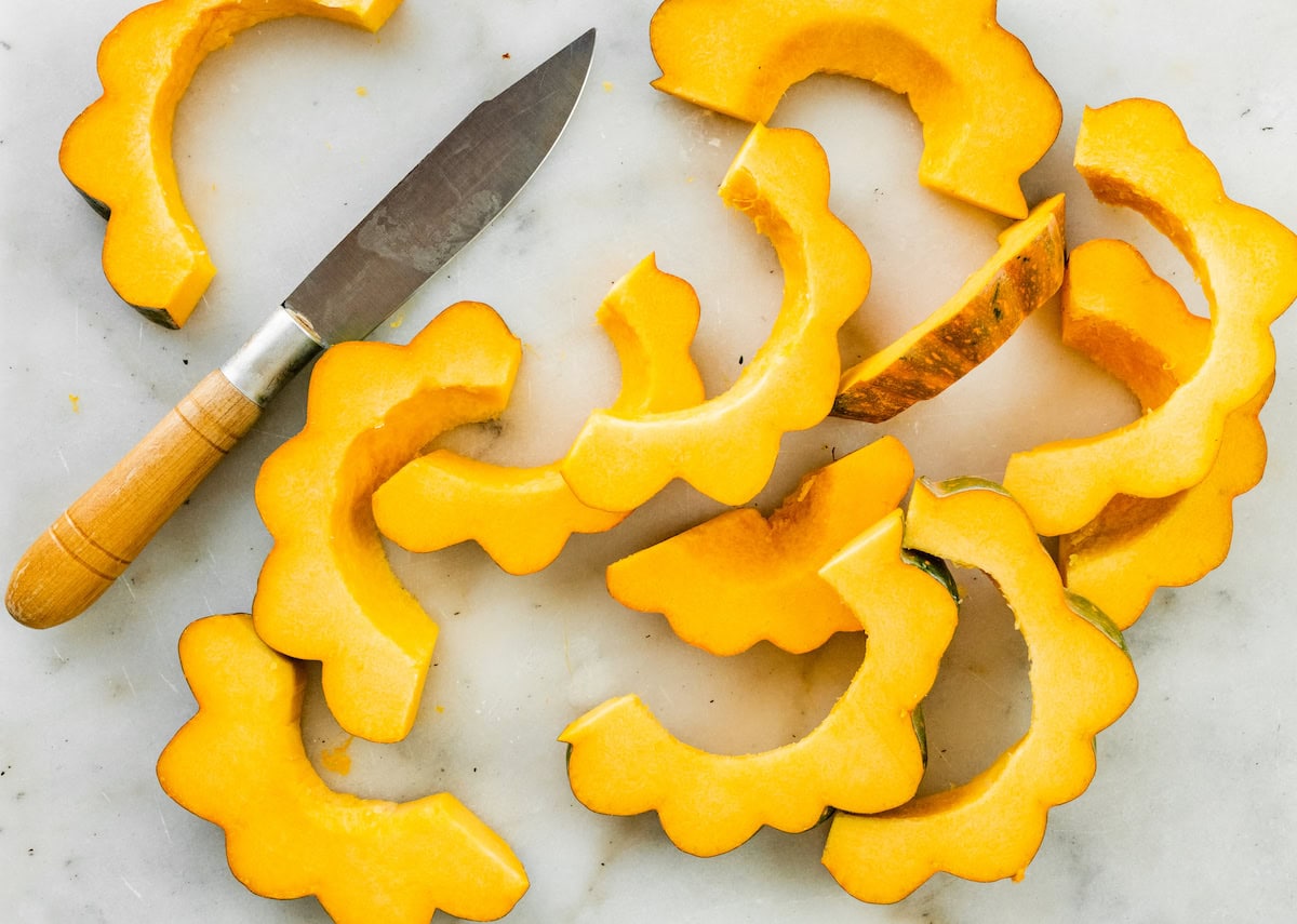 Acorn squash cut up on a cutting board with a knite.