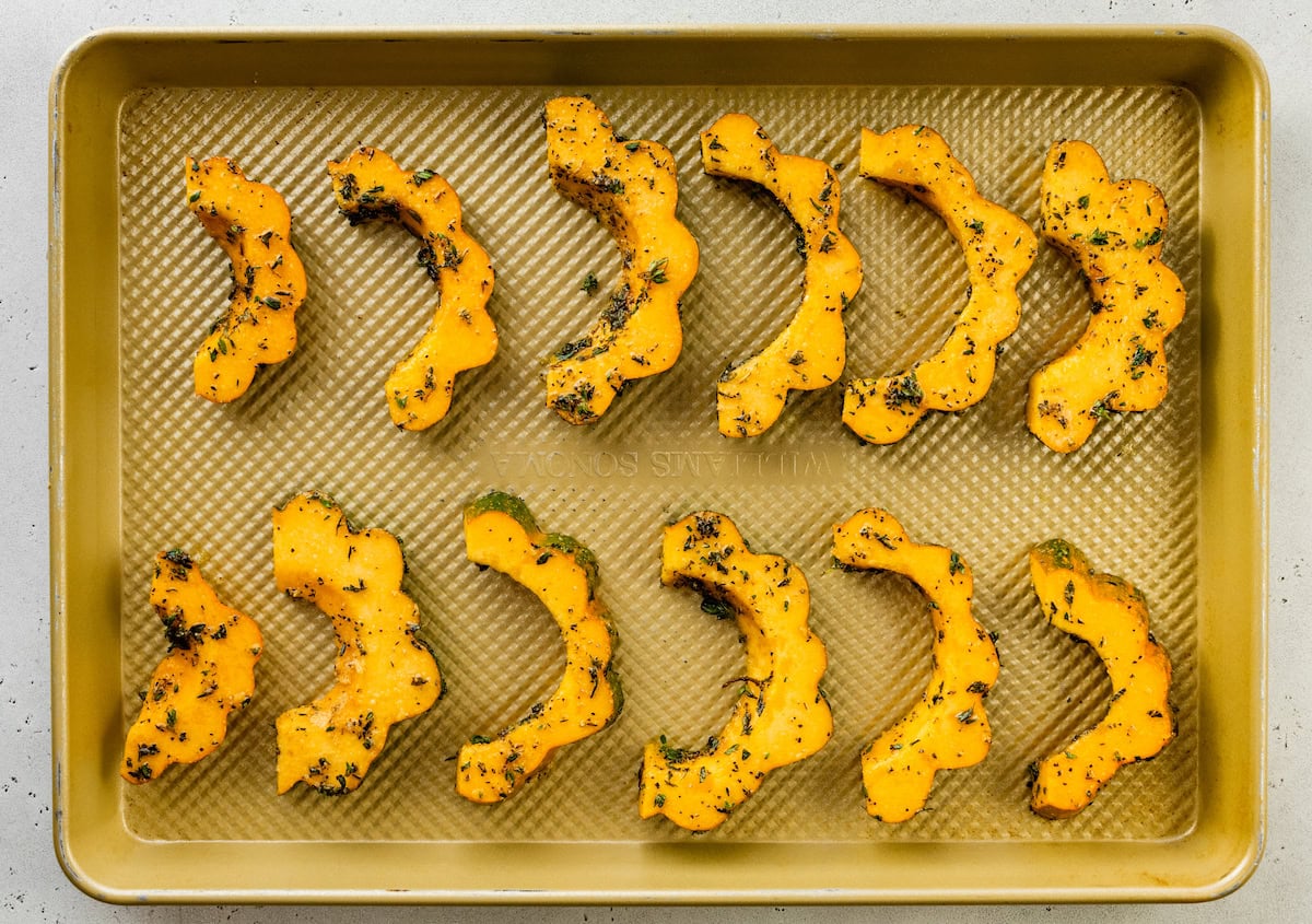 Acorn squash slices on a baking sheet before being roasted.