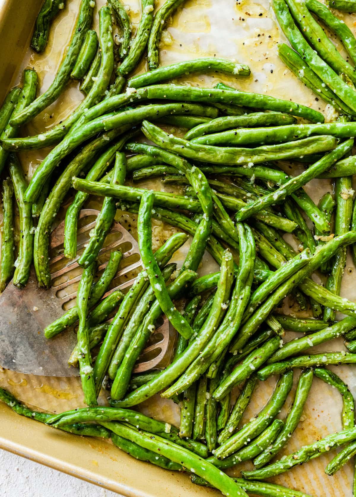 Roasted green beans on a baking tray with a metal spatula.